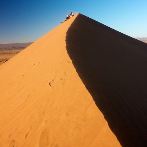 People sitting on top of dune watching sunset in Erg Chigaga desert