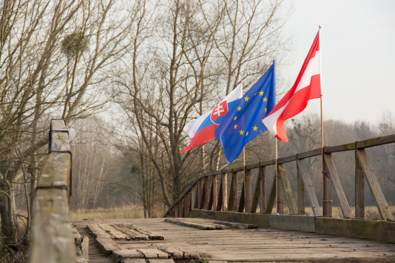 Detailní pohled na vlajky Slovenska, Evropské unie a Rakouska na dřevěném mostě k Pohansku.