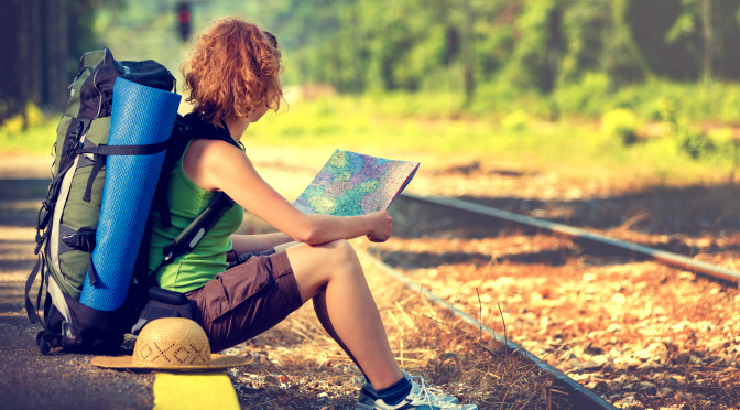 Cestovatelka s batohem a mapou v ruce, čekající na vlak.
